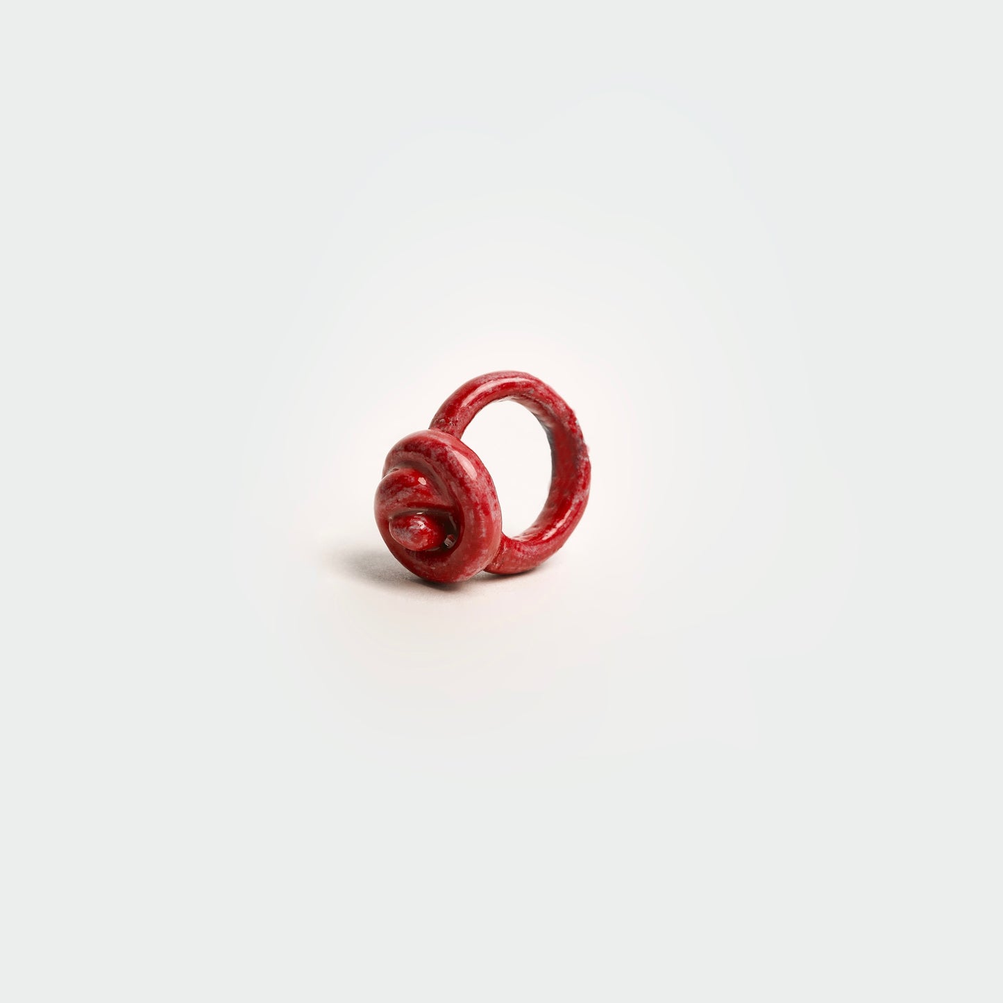 Anillo en fondo blanco hecho a mano en forma de merengue en materia de cerámica color rojo.