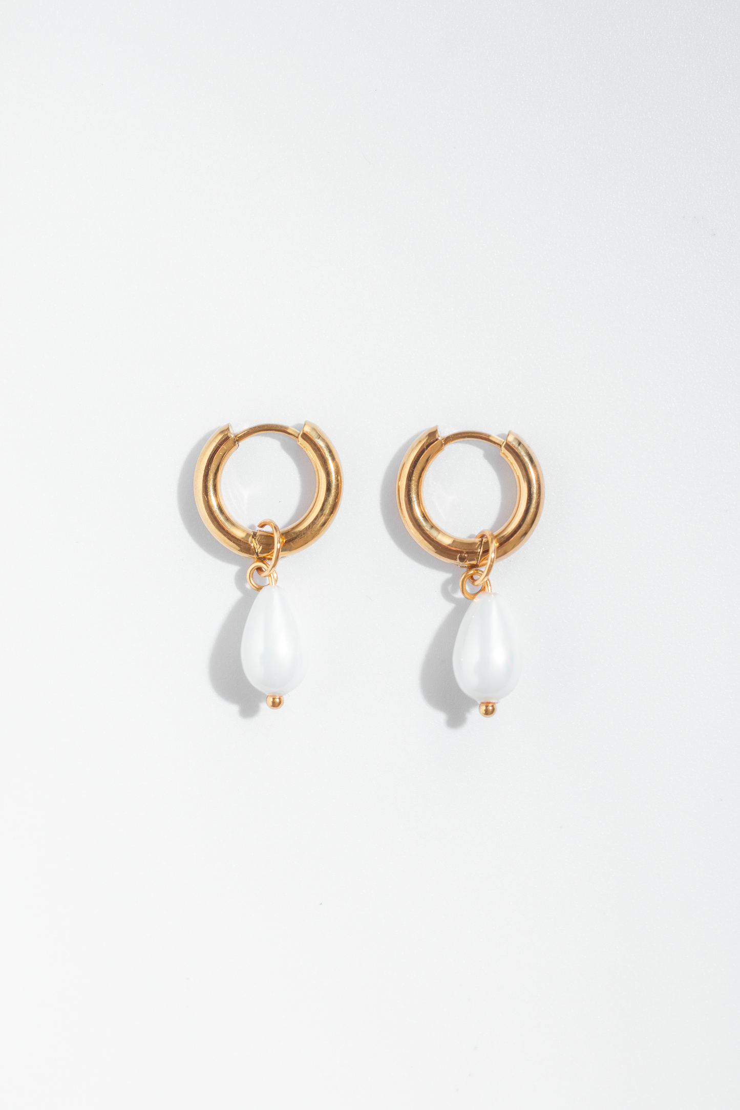 Aretes estilo candonga en material de acero inoxidable color dorado con dije colgante de perlas de polvo de nácar color blanco.