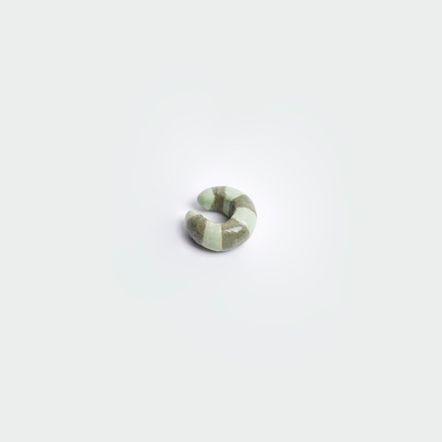 Earcuff en fondo blanco hecho artesanalmente en cerámica, estilo de rayas en colores verde claro y verde oscuro