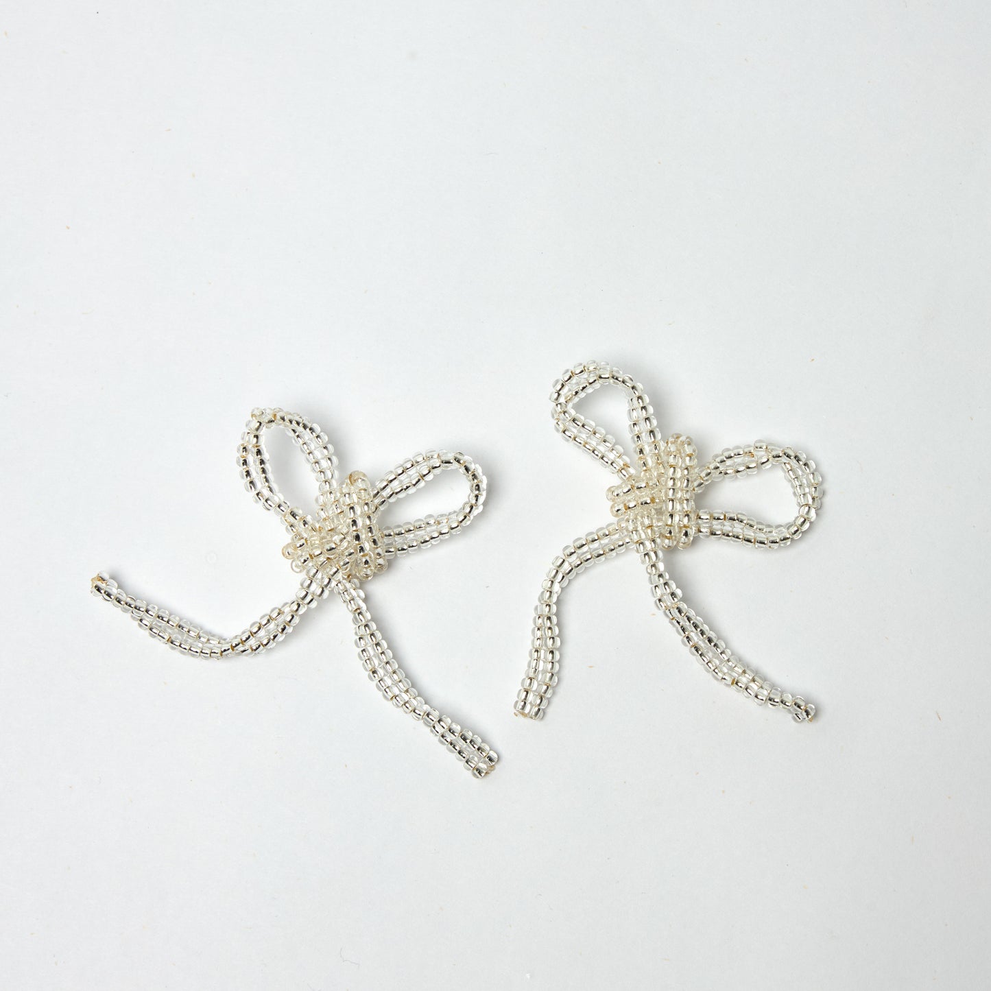 Aretes estilo coquette con base de pendiente en oro golfi con forma de moño en color transparente, tejidos a mano en material de mostacilla