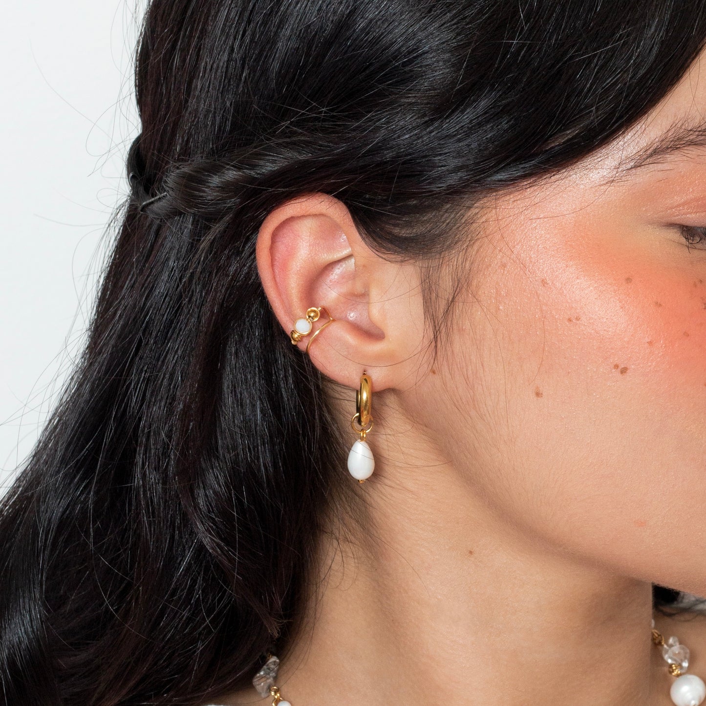 Oreja de modelo de tes blanca y cabello negro usando hoops medias noches con dije colgante de perla blanca, imagen tomada en fondo blanco.