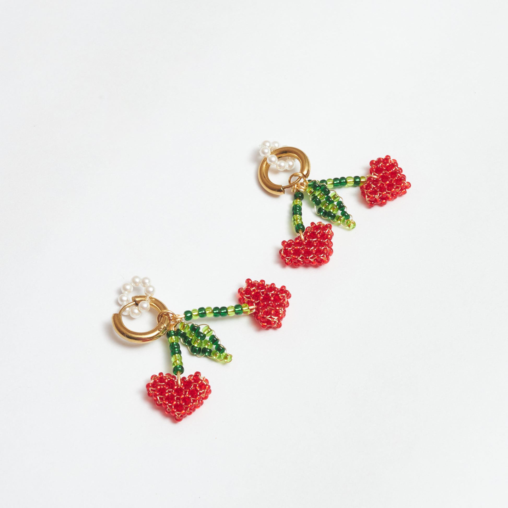 Aretes del set Berries estilo candonga en acero inoxidable color dorado con dijes en forma de cerezas tejidos artesanalmente en rocalla y mostacilla de colores verde claro, verde oscuro y rojo con alambre de oro golfi y dije de aro de perlas.