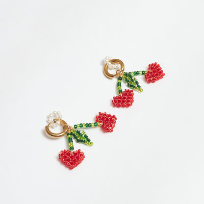 Aretes del set Berries estilo candonga en acero inoxidable color dorado con dijes en forma de cerezas tejidos artesanalmente en rocalla y mostacilla de colores verde claro, verde oscuro y rojo con alambre de oro golfi y dije de aro de perlas.