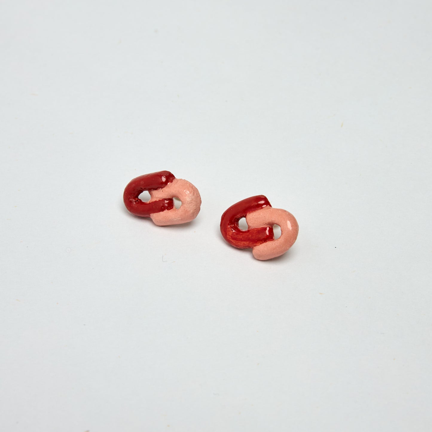 Aretes glimmers estilo topito con diseño de C entrelazada en material de cerámica con colores rojos y ladrillo
