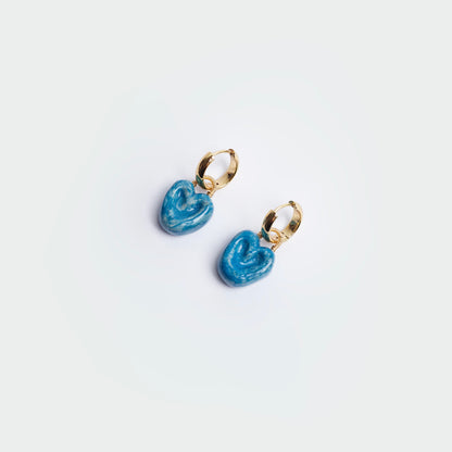 aretes colgantes estilo hoops en fondo blanco, hechos a mano en material de cerámica color azul con candongas en acero inoxidable color dorado.