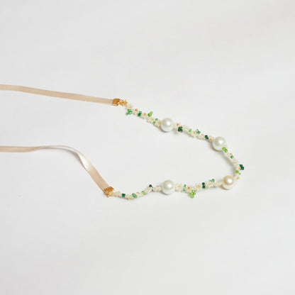 Collar estilo chocker tejido a mano en mostacilla rocaya y múranos brillantes en forma de flores en colores verde claro, verde oscuro, blanco y dorado y cintillas anudadas en forma de moño.
