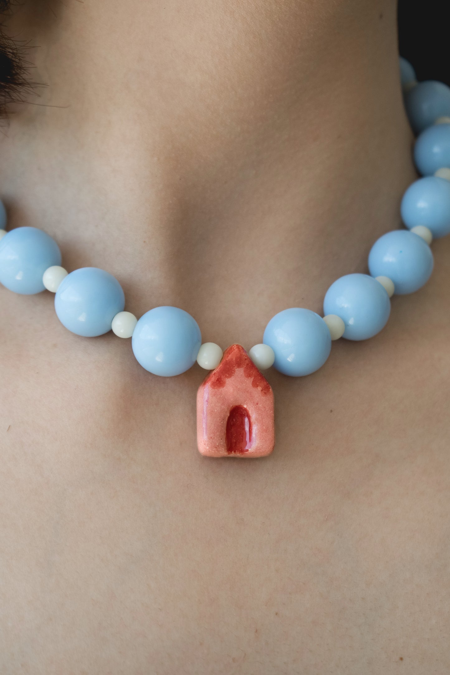 Cuello de modelo de tes blanca con collar La Casita con dije en cerámica porcelana con forma de casa en colores rojo y ladrillo.