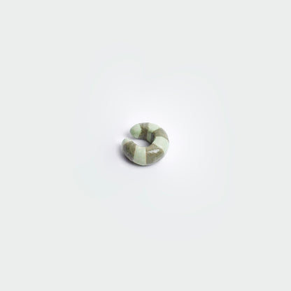 Earcuff en fondo blanco hecho artesanalmente en cerámica, estilo de rayas en colores verde claro y verde oscuro