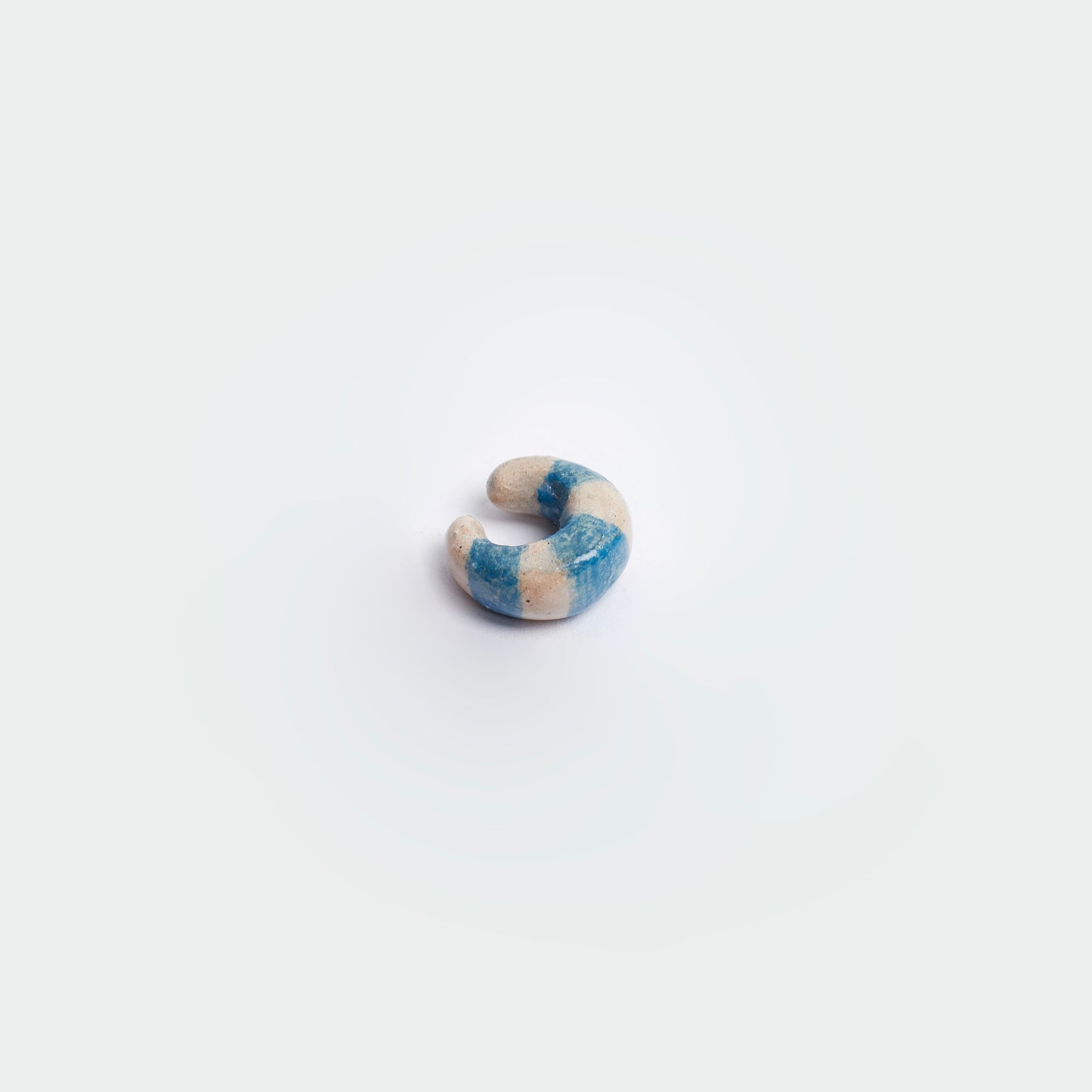 Earcuff en fondo blanco hecho a mano en material de cerámica en estilo de rayas color blanco y azul.