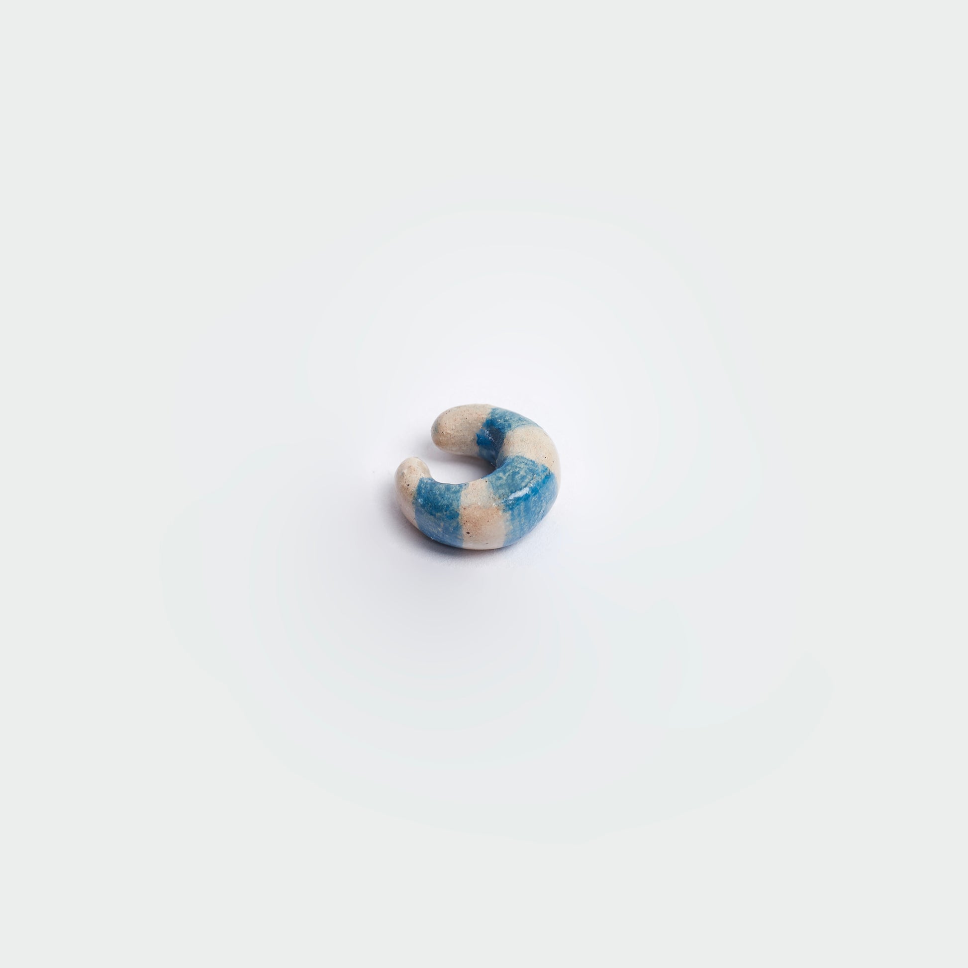 Earcuff en fondo blanco hecho a mano en material de cerámica en estilo de rayas color blanco y azul.