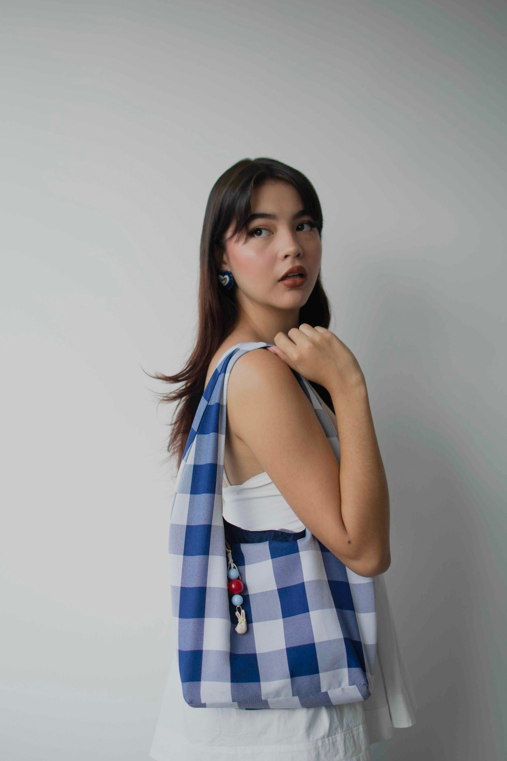 Modelo de tes blanca y cabello negro usando bolso estilo tote bag con charm bag con dije en cerámica y forma de conejo atado a un extremo 