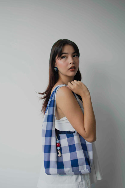 Modelo de tes blanca y cabello negro usando bolso estilo tote bag con charm bag con dije en cerámica y forma de conejo atado a un extremo 