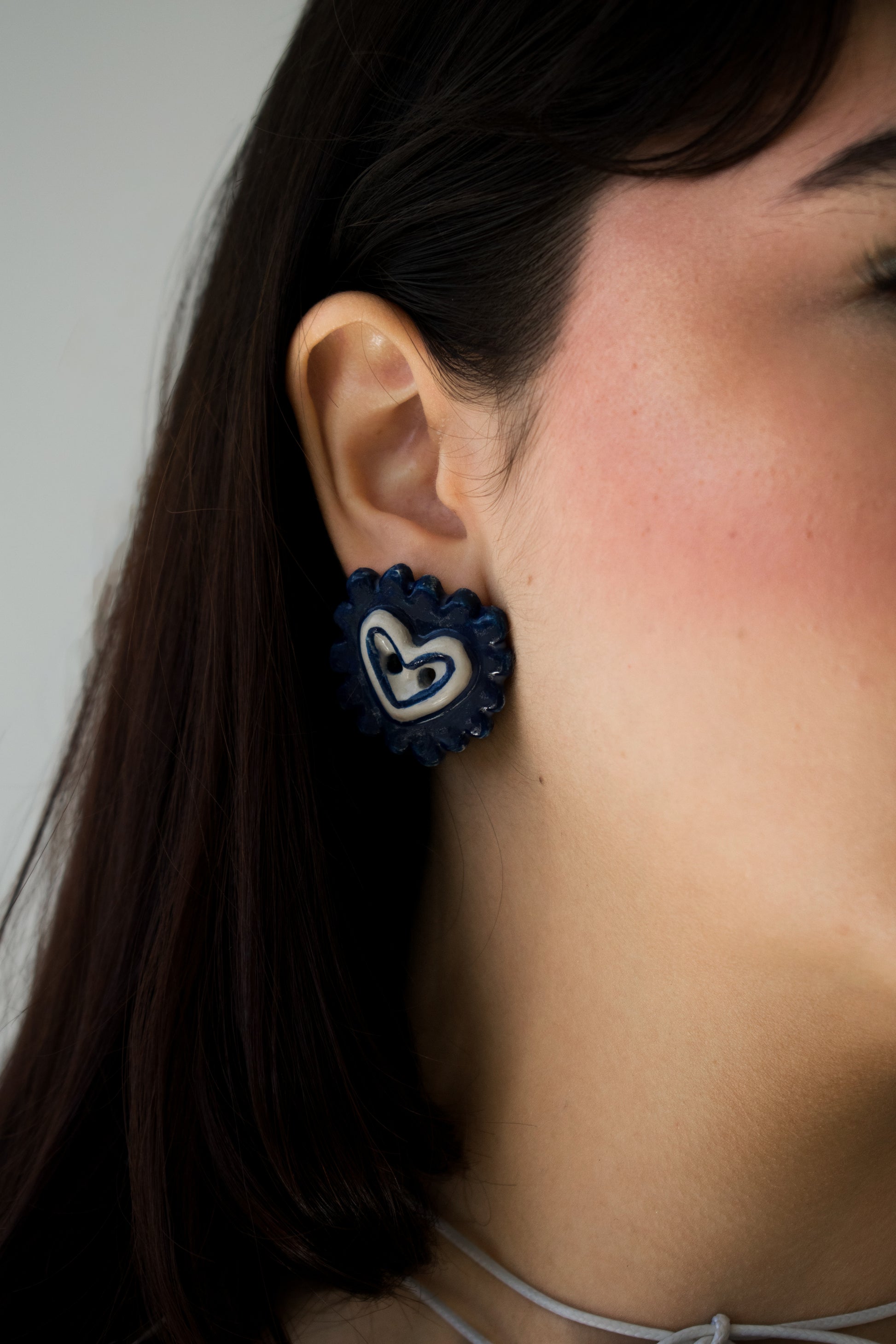 Modelo de tes blanca y cabello negro con vestido blanco y arete la galletera estilo pendiente en material de cerámica, foto tomada en fondo blanco
