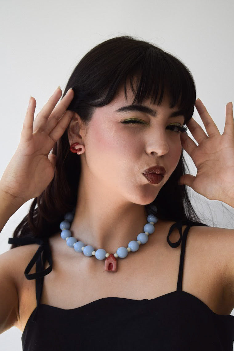 modelo delgada de tes blanca y cabello negro con vestido negro y juego de accesorios que incluye collar maximalista de casa y aretes de cerámica porcelana