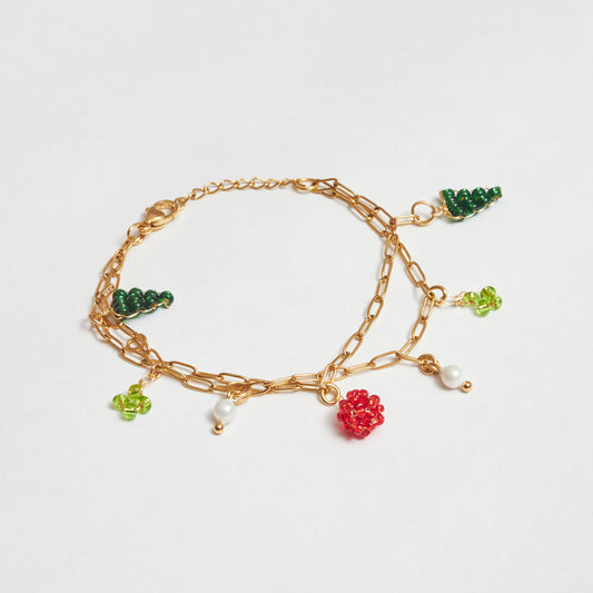 Brazalete doble de cadena en material de acero inoxidable color dorado con dijes de perlas blancas y en mostacilla tejida con forma de árbol, flor y fruto rojo en colores verde claro, verde oscuro y rojo.